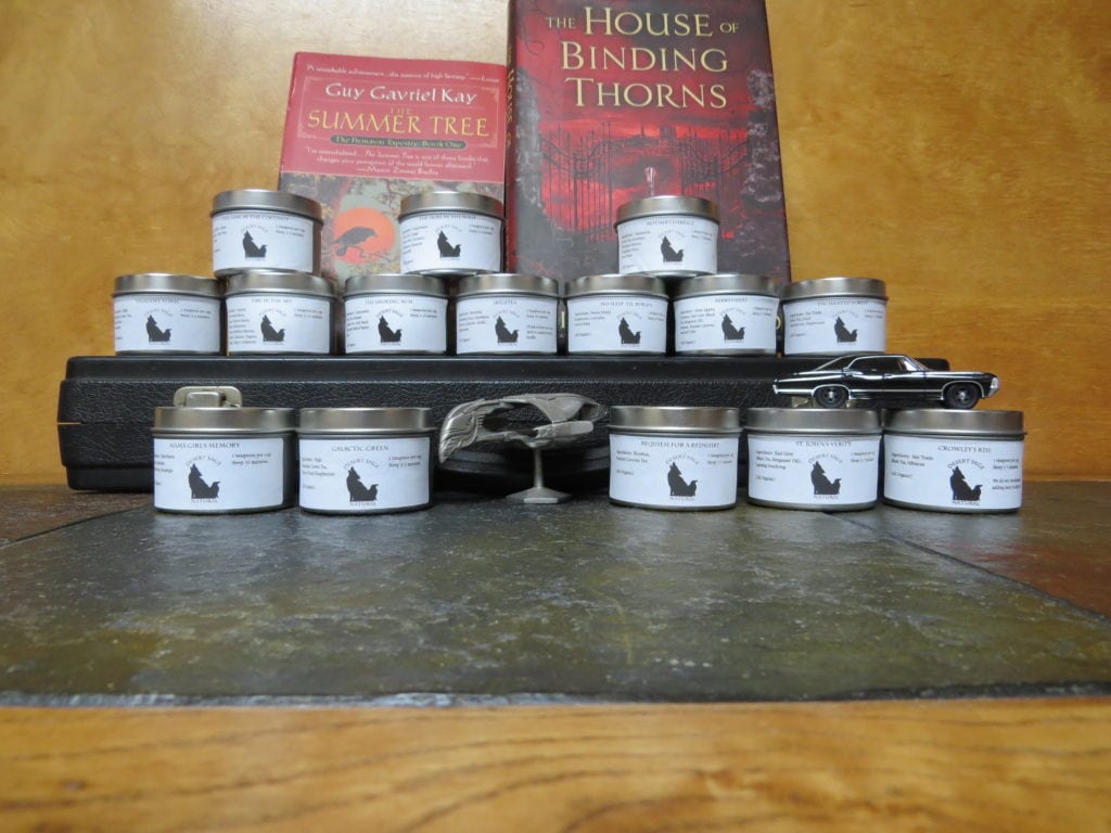 An array of tea tins, on and around a flute case. A Bird of Prey and the Winchester's car pose with the teas. Behind the top row are two books.