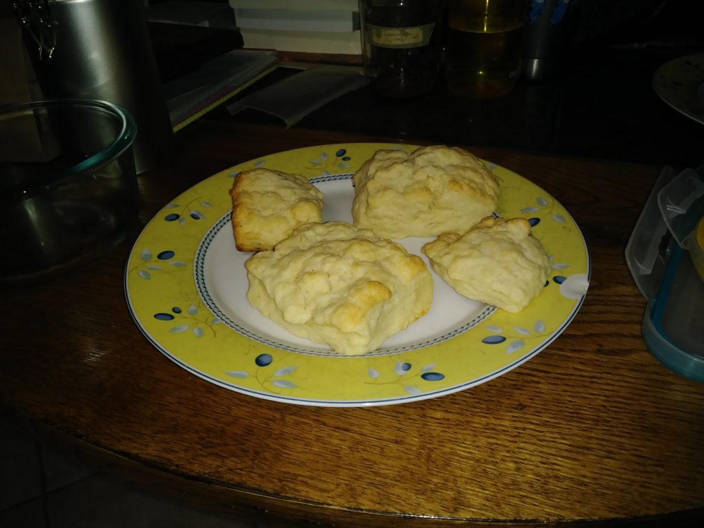 4 biscuits, on a plate with a white center, the outer edge has a circle of yellow, with blueberries and leaves.