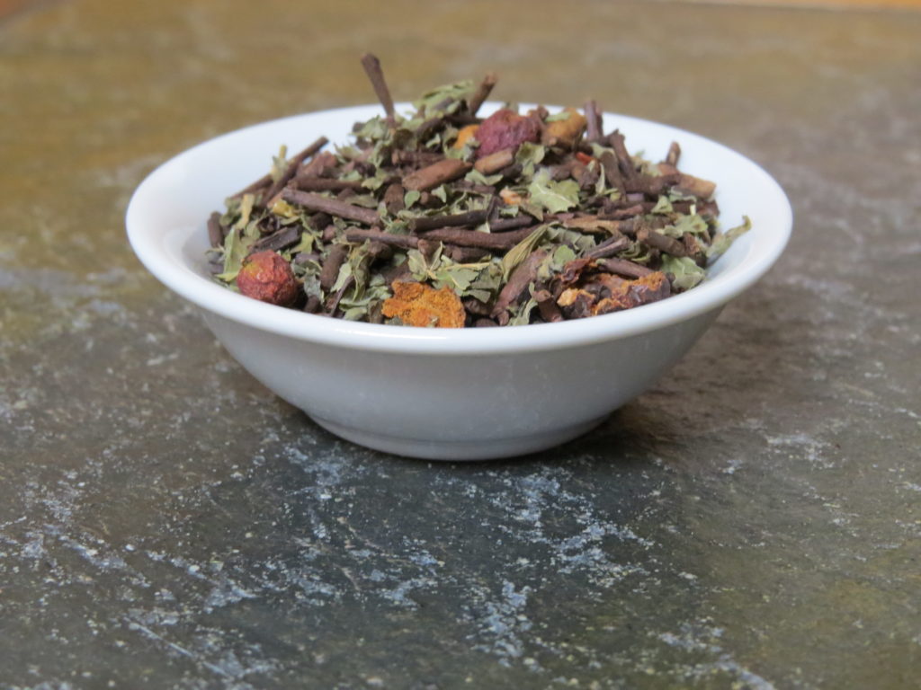 A small white bowl on a textured green marble table full of a blend of roasted kukicha, hawthorn berries, and lemon balm.